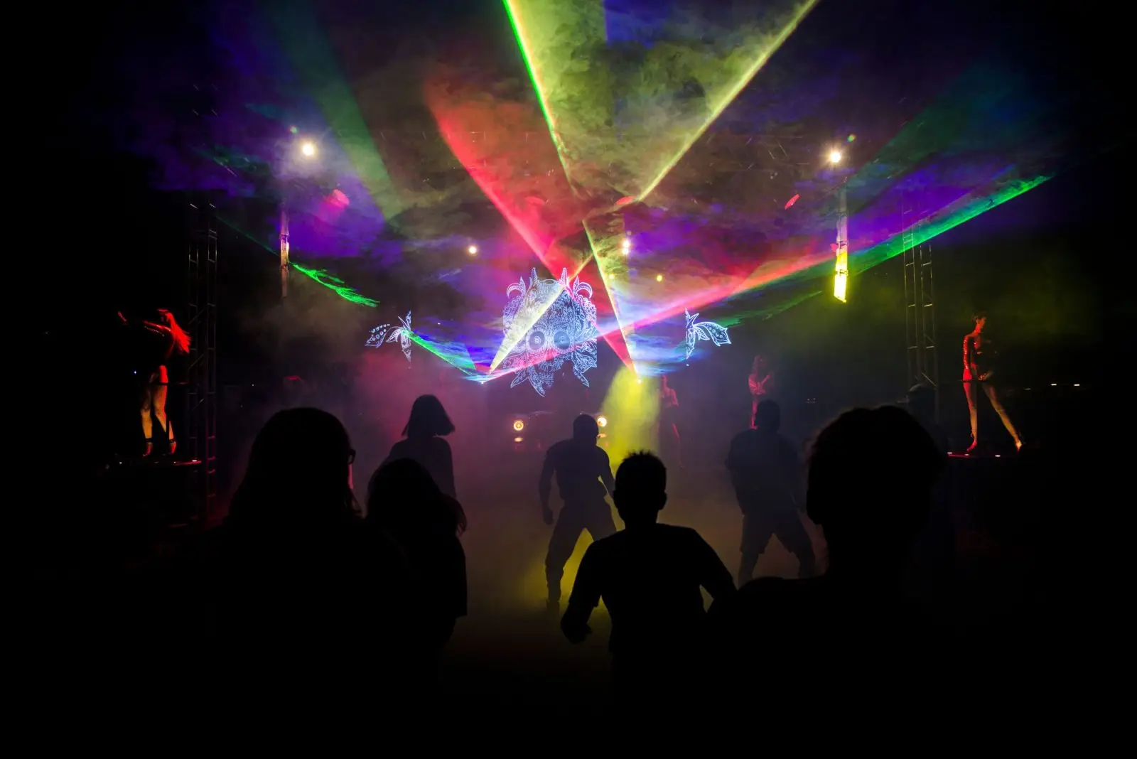 Silhouettes dance amid colorful laser lights in a vibrant nightclub setting.